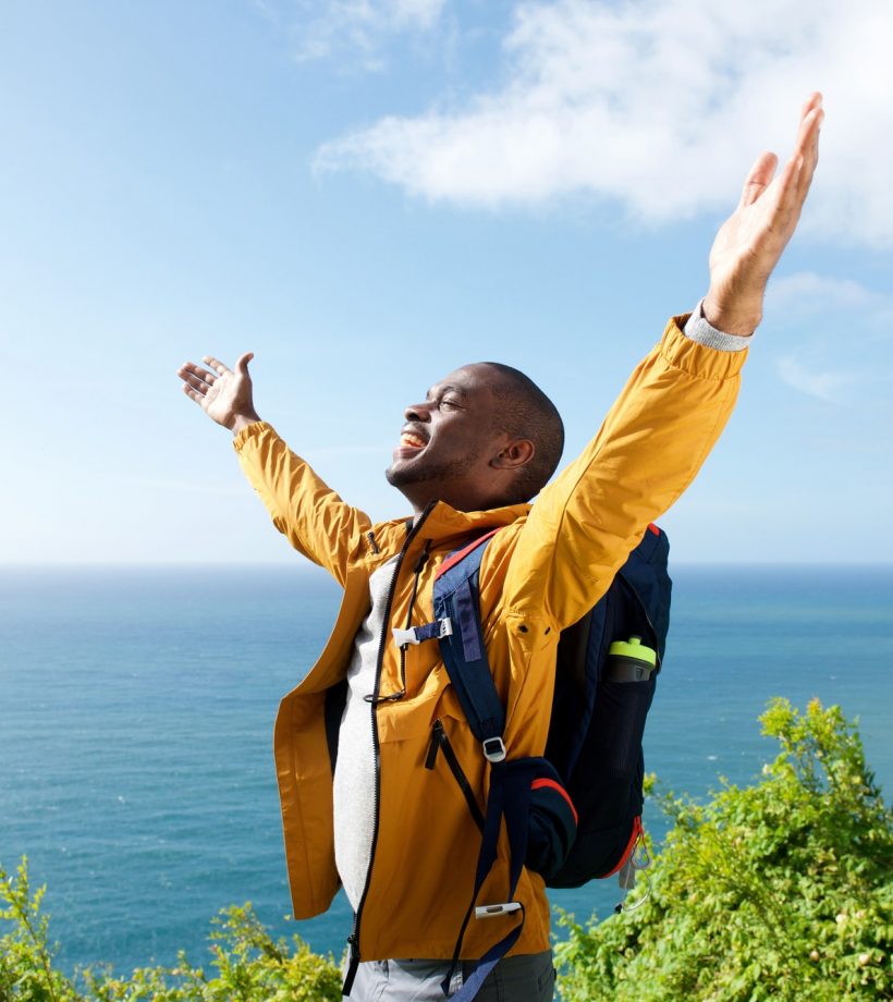 happy young african american male traveler with arms open outdoors
